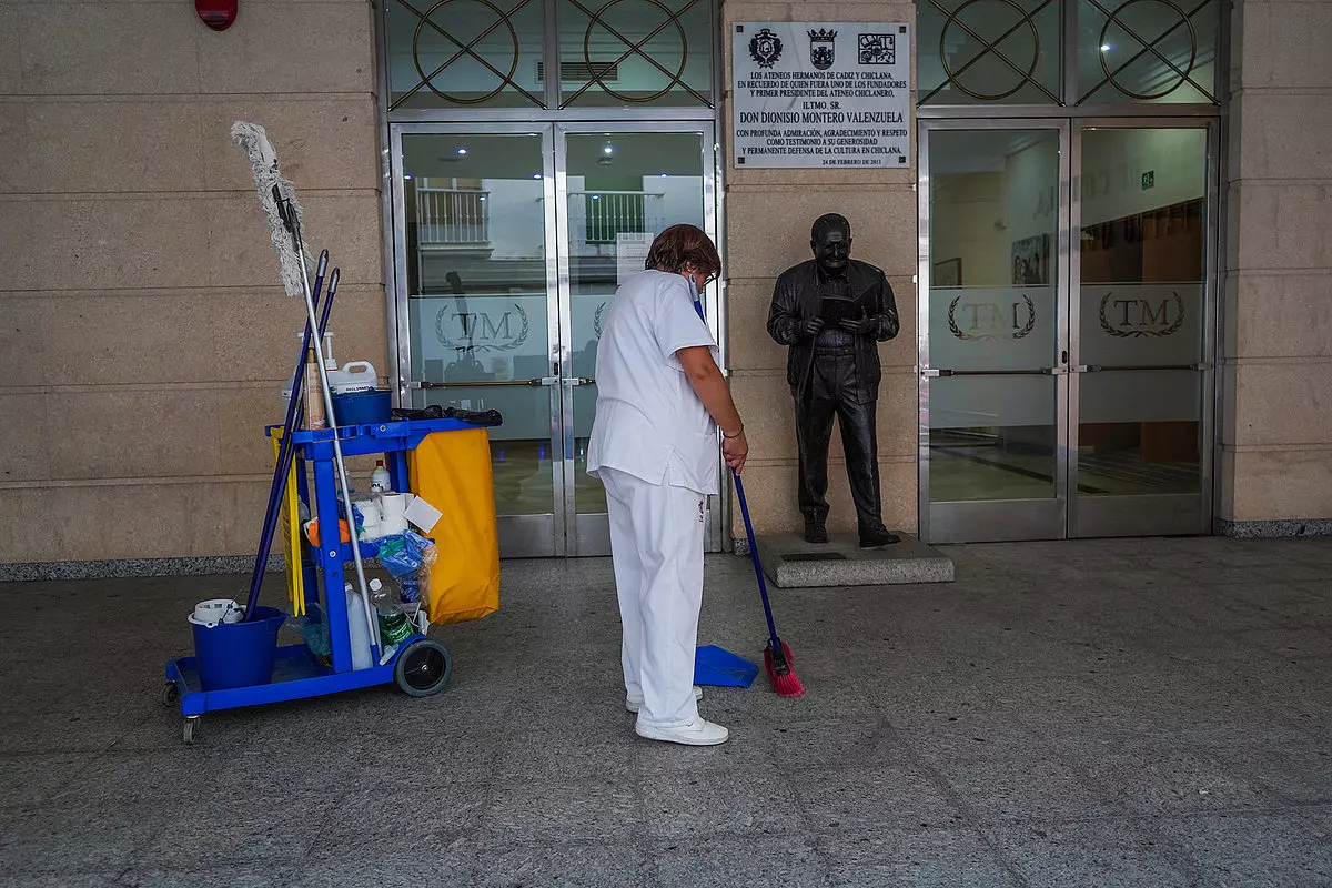 Persona limpiando entrada con escultura y carrito de limpieza